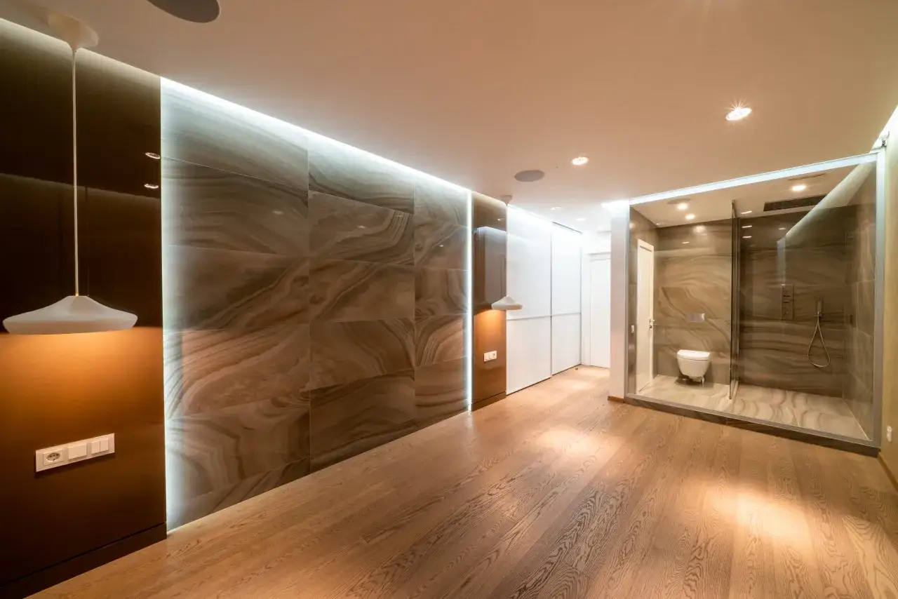 Bagno moderno con doccia in cristallo e WC, pareti in marmo e illuminazione integrata. Pavimento in legno e lampada di design completano lo stile minimal.