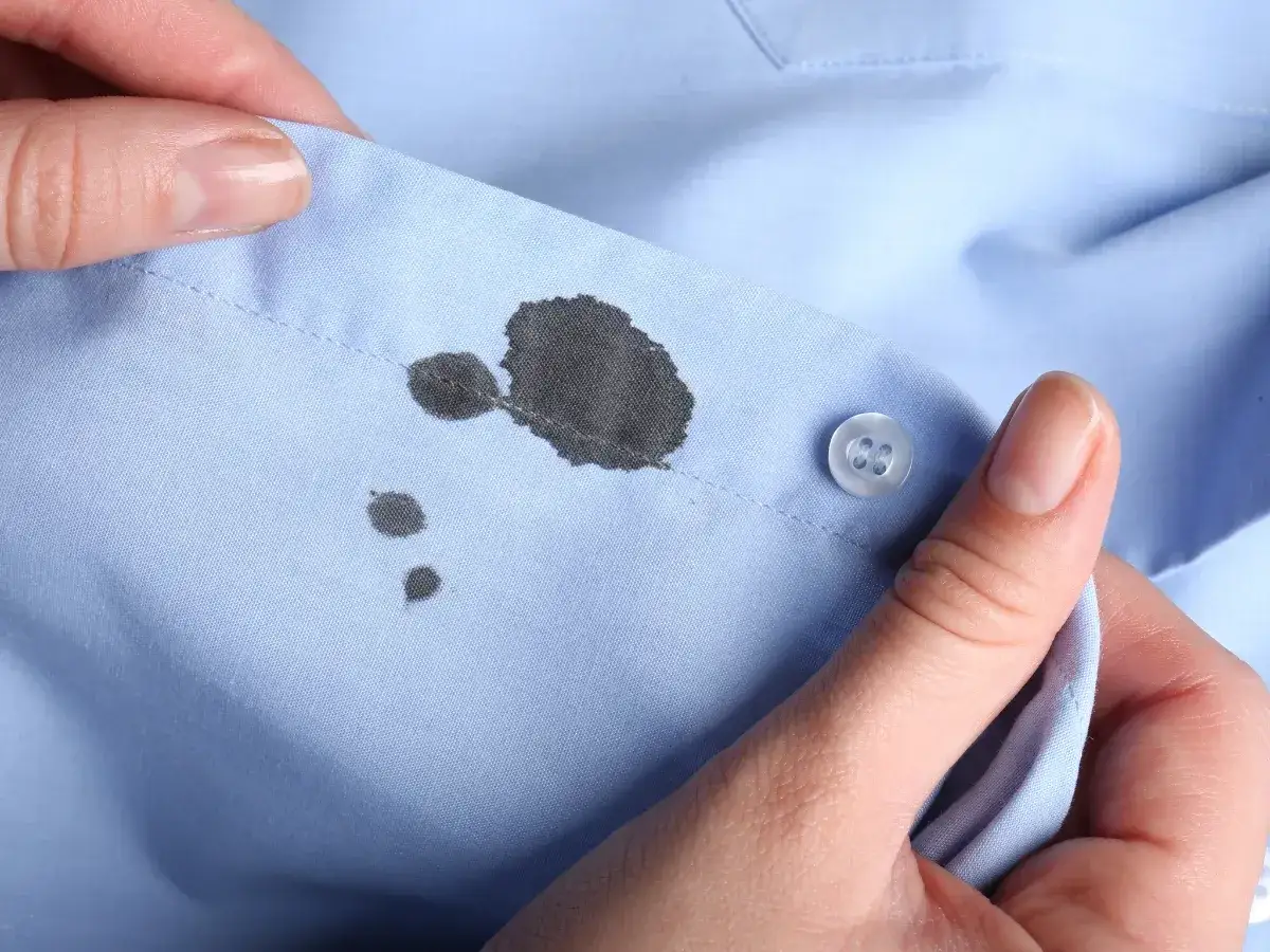 Manos sostienen camisa azul con manchas de bolígrafo. Aprende como quitar manchas de bolígrafo en ropa.