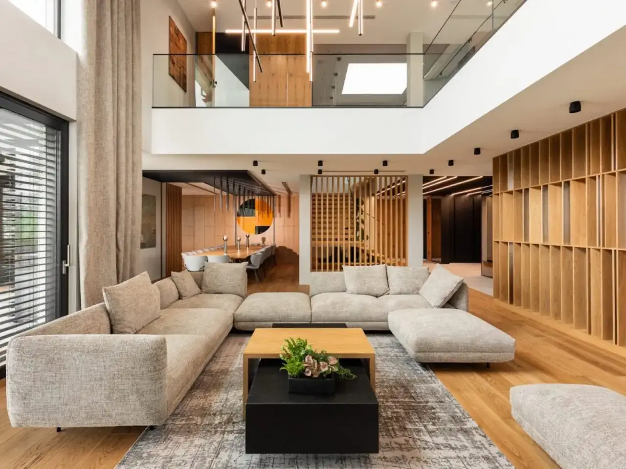 Nowoczesny, minimalistyczny salon z wygodną, narożną sofą, drewnianymi elementami i designerskim oświetleniem.