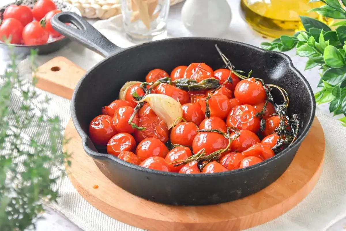 Tomates cherry confitados en sartén de hierro fundido con ajo y hierbas.