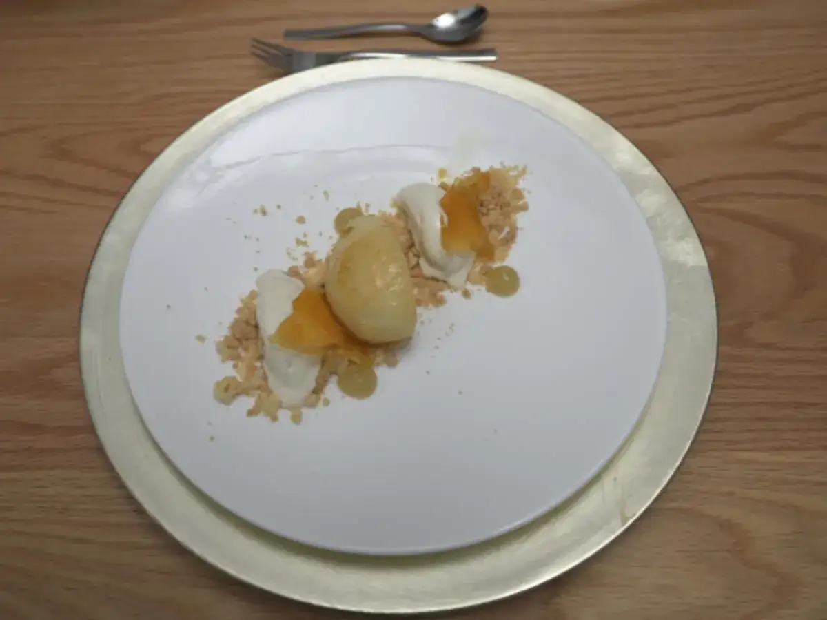 Ein kunstvoll angerichtetes Dessert mit Crema Catalana Eis, zerbröseltem Keks und karamellisierten Früchten auf einem weißen Teller.