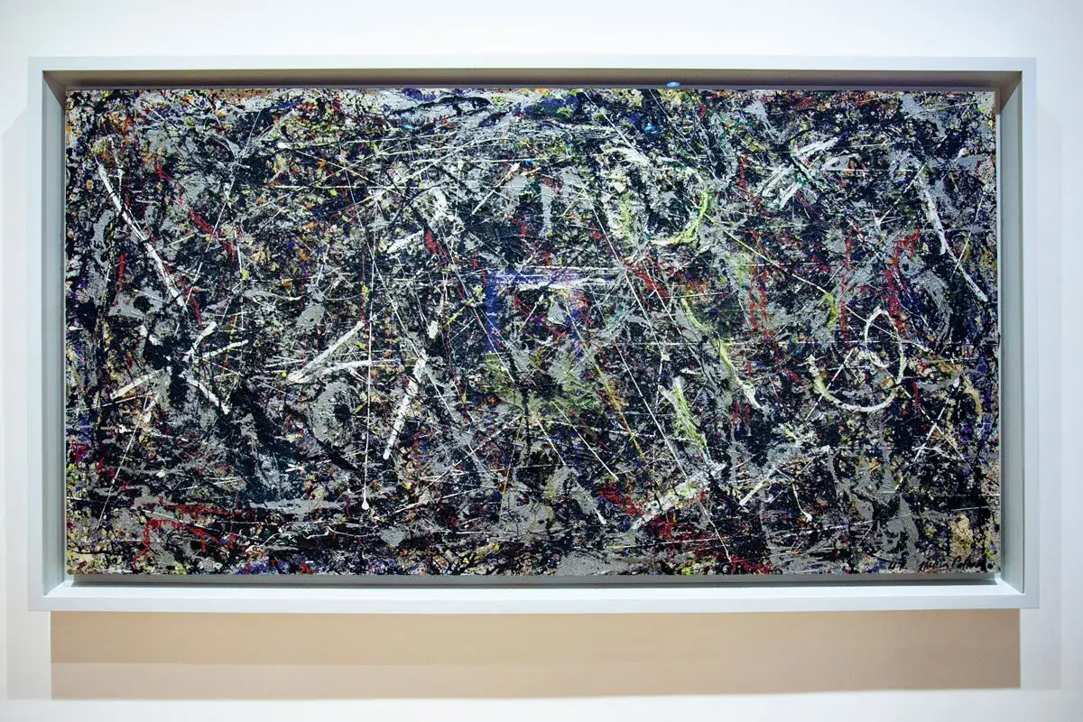 Un'opera di Peggy Guggenheim a Venezia: un dipinto astratto con schizzi di vernice bianca, nera, rossa e gialla su sfondo grigio.