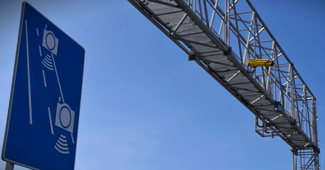 Niebieski znak informuje o odcinkowym pomiarze prędkości S7. Nad drogą widać konstrukcję z żółtą kamerą.