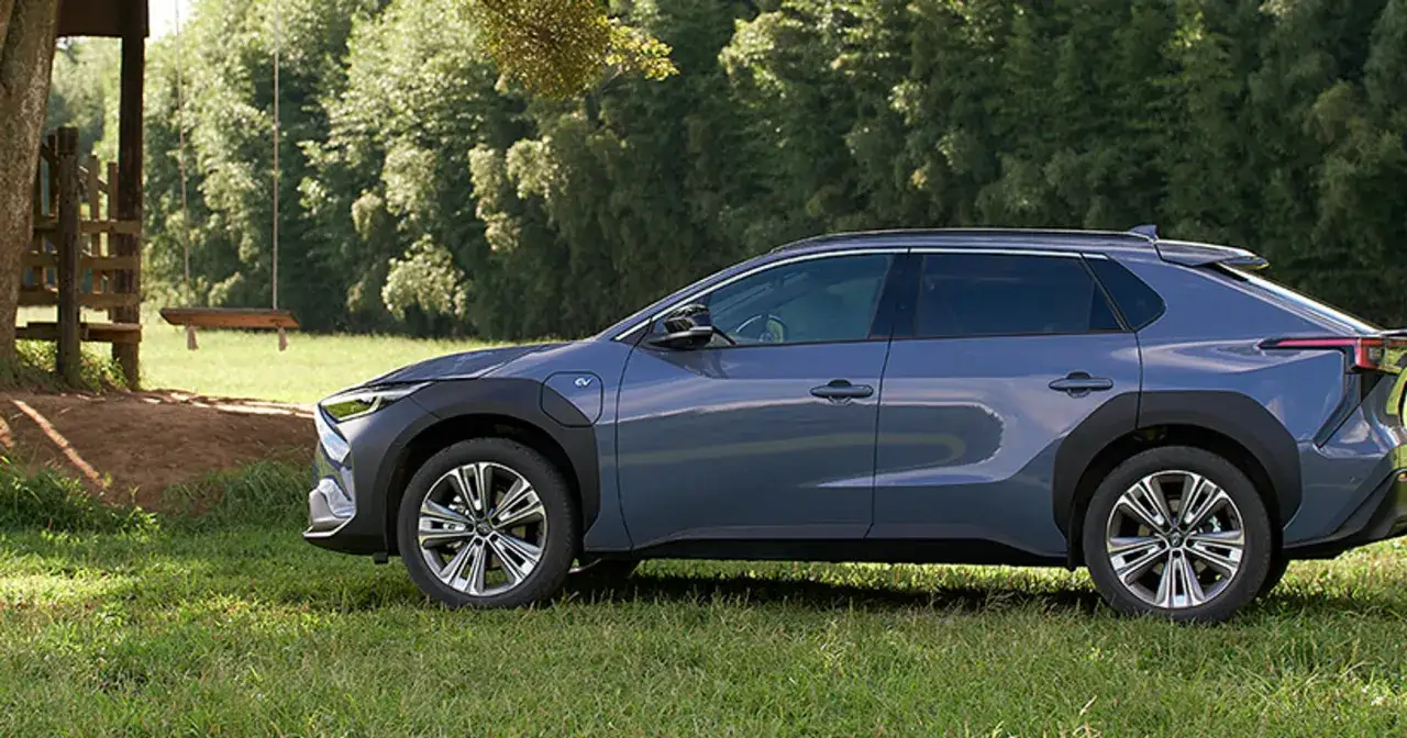 Subaru Solterra, elektryczny SUV, zaparkowany na trawie obok drewnianej huśtawki i drzew.
