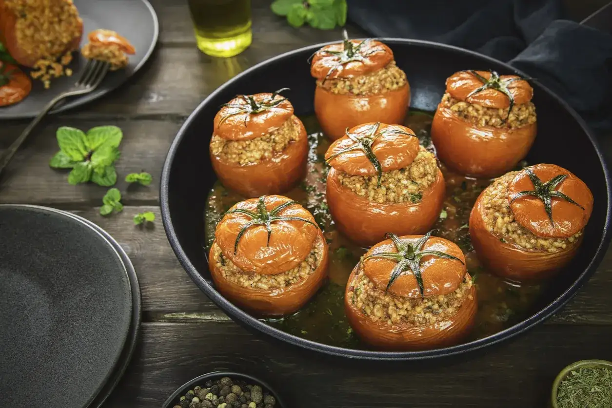 Six tomates farcies, garnies de riz et d'herbes, baignent dans une sauce savoureuse dans une poêle.