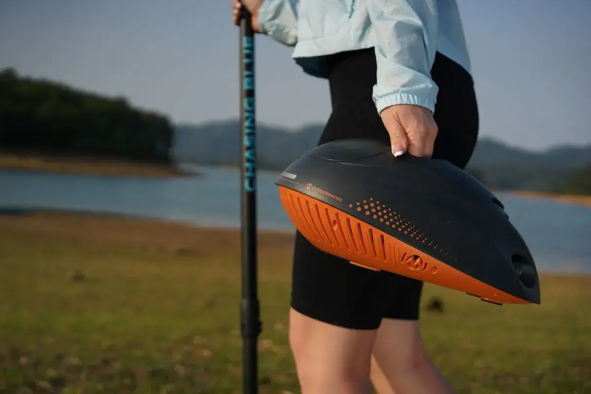 Person h&auml;lt eine Pumpe f&uuml;r SUPs am See. Der sup luftdruck ist perfekt f&uuml;r den Ausflug.