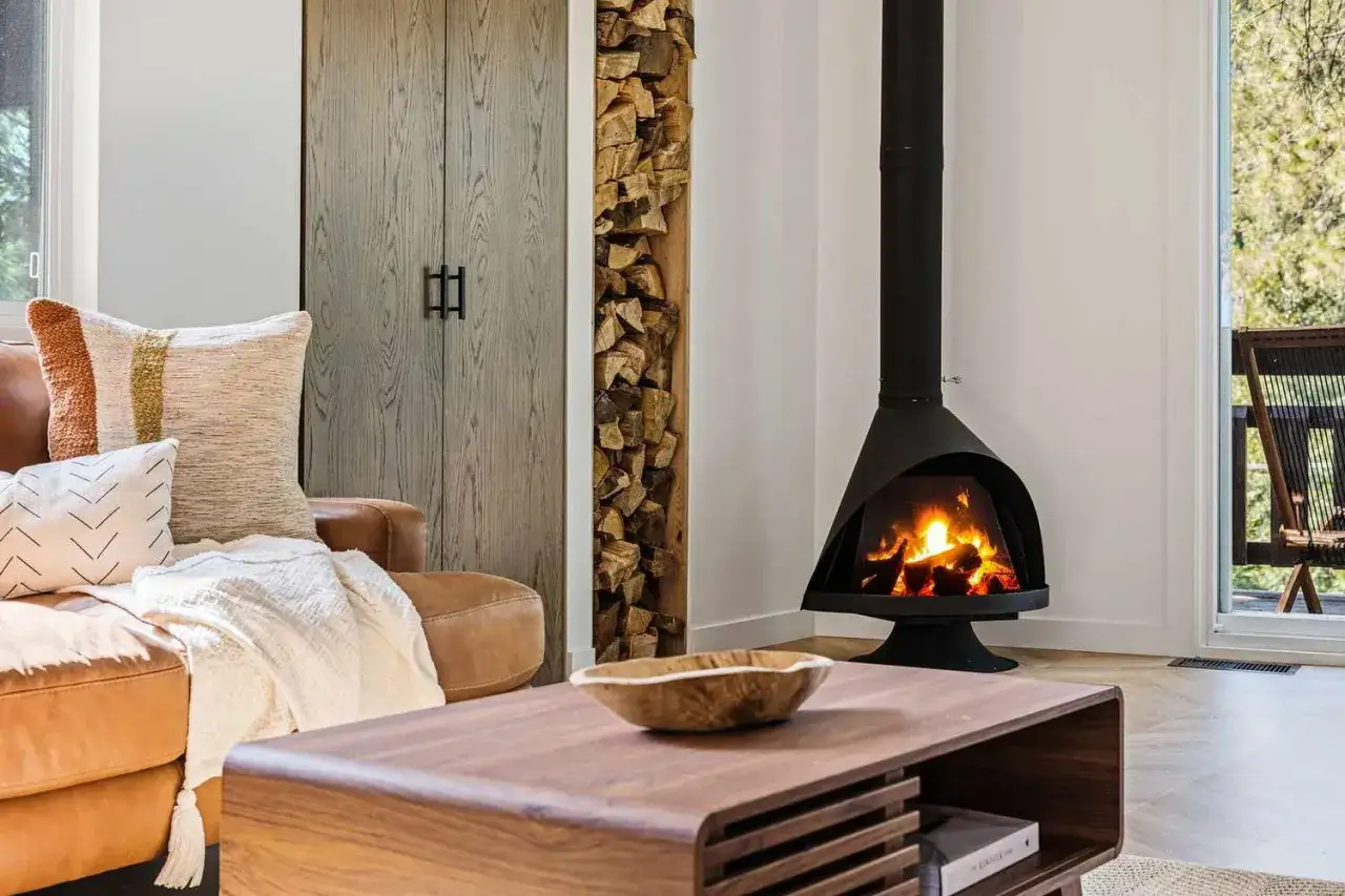 Gemütliches Wohnzimmer mit Kaminfeuer und Holzstapel. Eine moderne Pellet-Hybridheizung sorgt für wohlige Wärme.