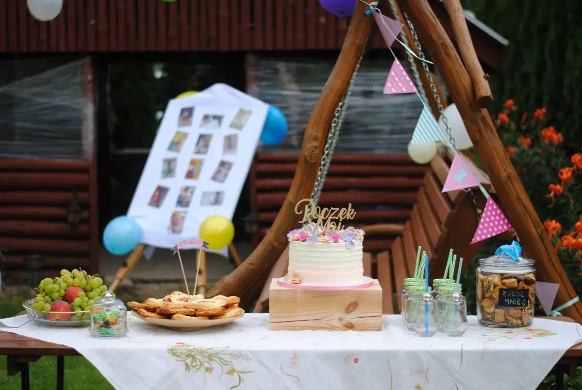 Uroczy tort i przekąski na pierwsze urodziny w domu. W tle tablica ze zdjęciami i balony.