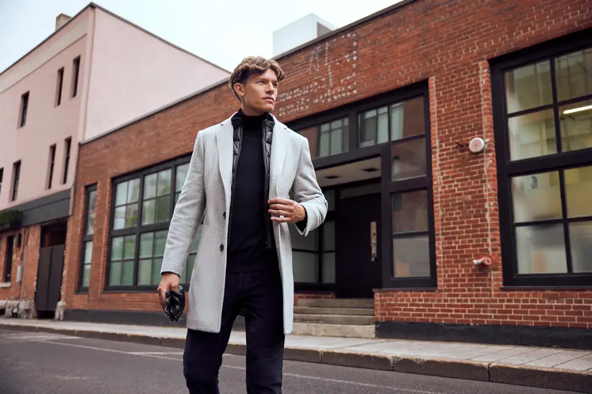 Mann im eleganten Mantel, schwarzem Rollkragenpullover und Jeans – ein perfekter **dresscode chic herren** für die Stadt.