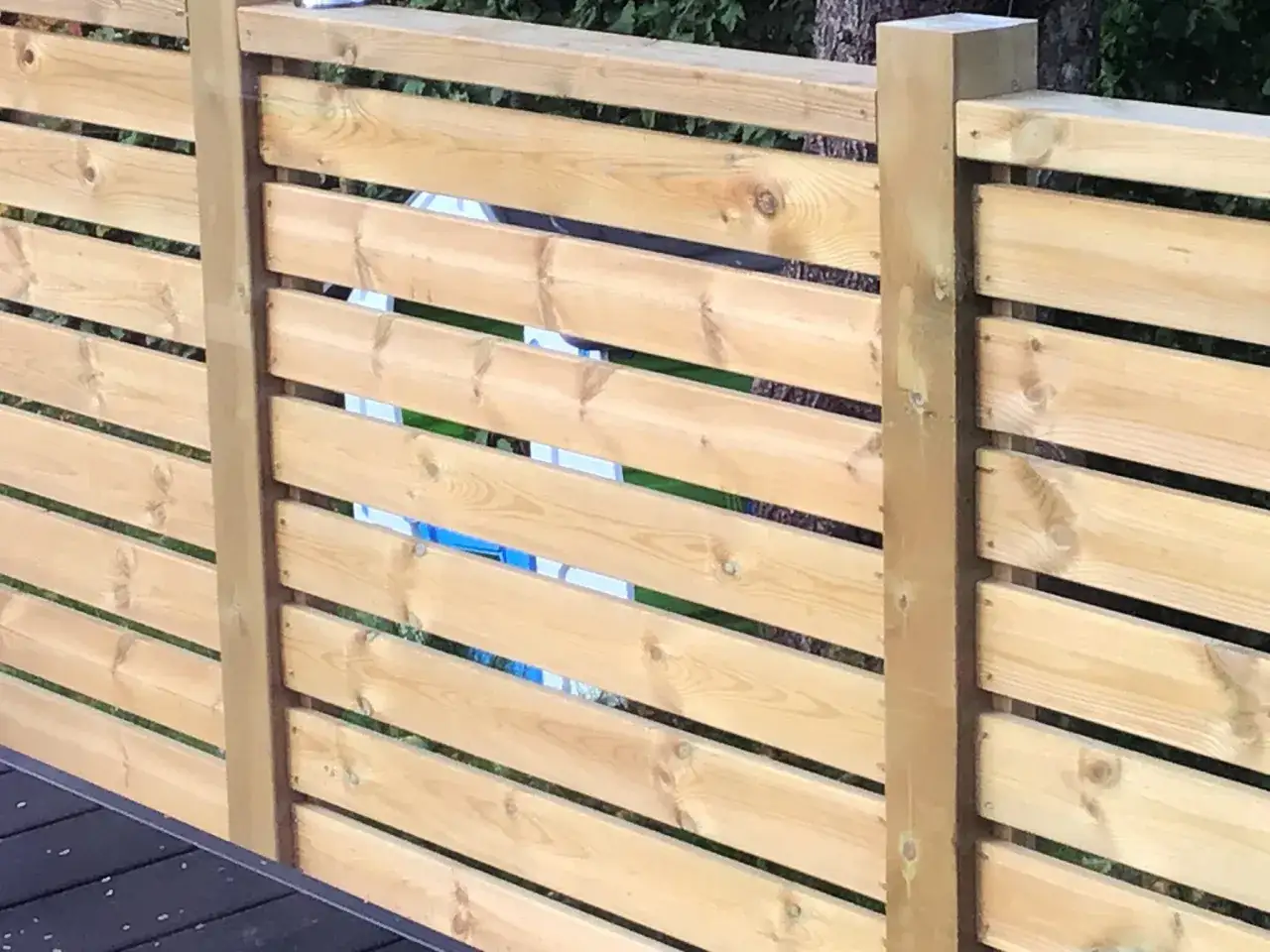Staket med liggande ribbor av olika bredd, monterade p&aring; tr&auml;stolpar.