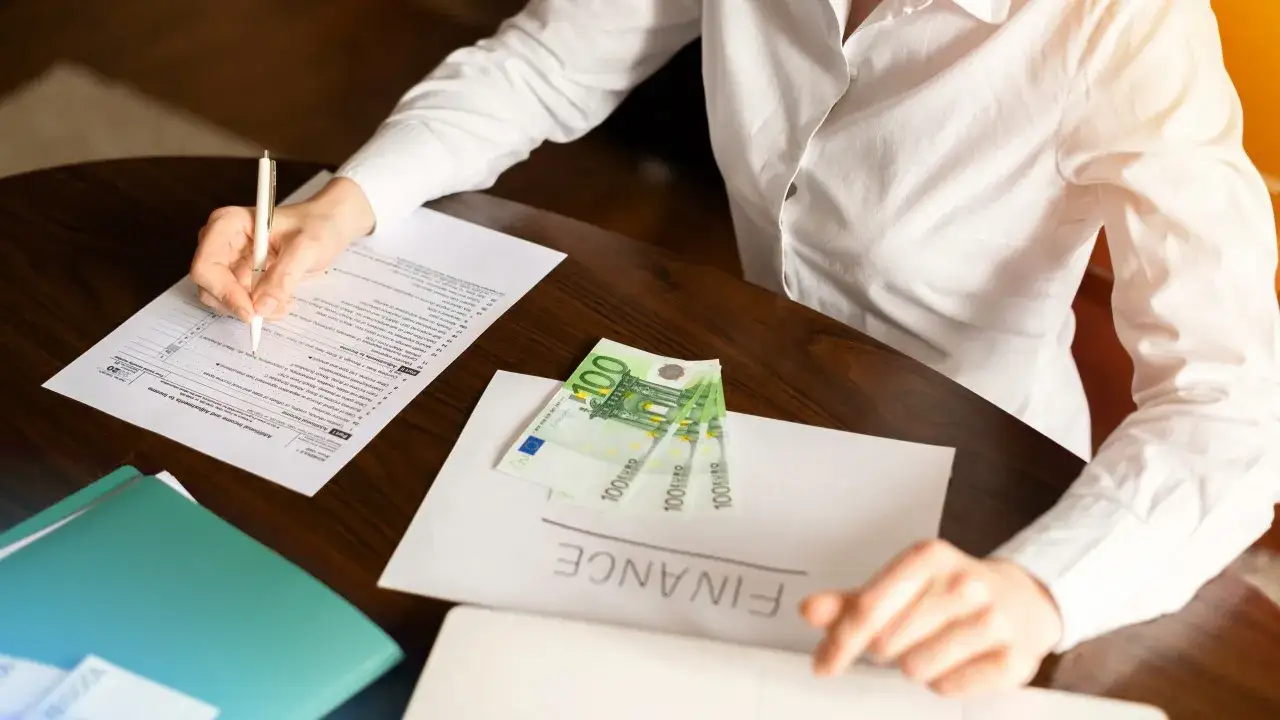 Kobieta wypełnia dokumenty finansowe, na stole leżą banknoty euro. Zastanawiasz się, ile trwa uruchomienie kredytu hipotecznego?