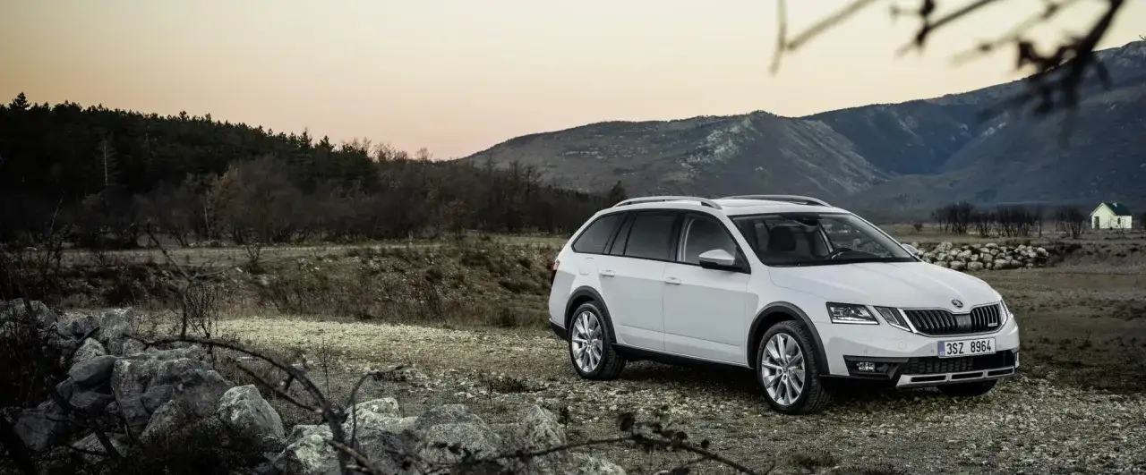 Vit Skoda Octavia Scout står parkerad på en grusväg med berg och skog i bakgrunden. Kanske ett problem med att hitta vägen?