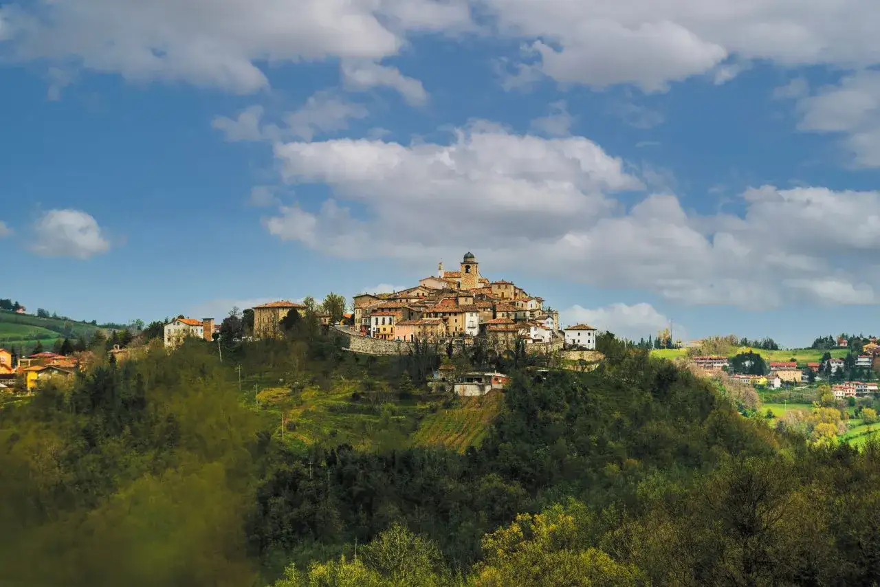 Borgo medievale arroccato su una collina, con case in pietra e tetti rossi. Il **monte Grimano** domina il paesaggio verdeggiante sotto un cielo azzurro con nuvole bianche.