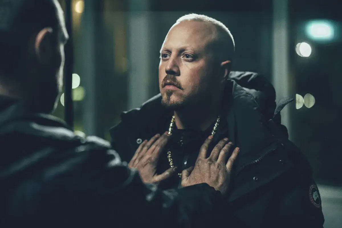 En intensiv scen fr&aring;n en sebbe stakset film. Tv&aring; m&auml;n m&ouml;ts i m&ouml;rkret, en med guldkedja, den andra med h&auml;nderna p&aring; hans br&ouml;st.