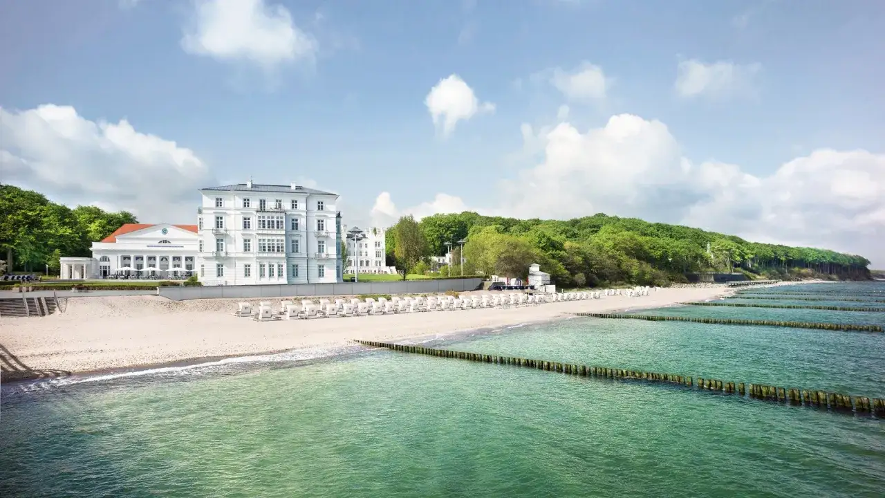Vit strand med vita strandstolar, gr&ouml;nt hav och en vit byggnad vid den tyska rivieran.