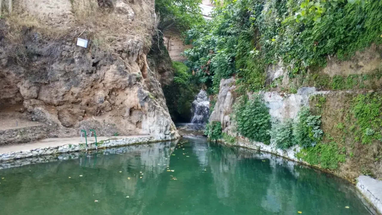 Un remanso de paz en las piscinas naturales de Albacete. Agua cristalina rodeada de rocas y vegetación exuberante, con una pequeña cascada al fondo.