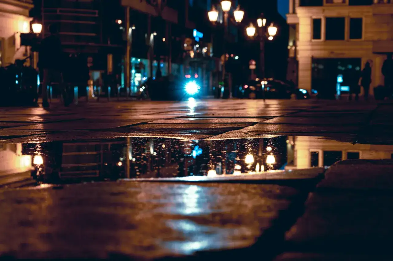 Une rue de ville la nuit, avec des reflets de lumi&egrave;res dans une flaque d'eau. Belles photos sous la pluie, ambiance urbaine et nocturne.