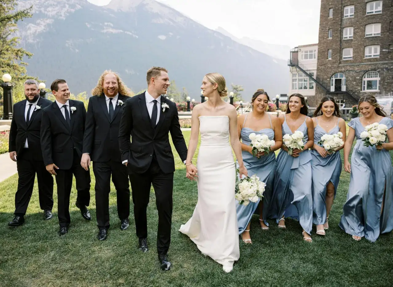 The groomsmen match the groom in black suits, walking with the bride and bridesmaids in blue dresses.