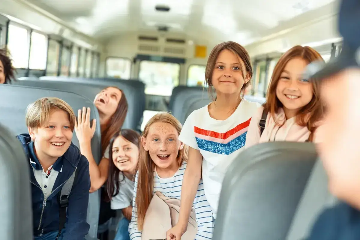 Uśmiechnięte dzieci w autobusie szkolnym. Warto wiedzieć, na co można przeznaczyć środki z dotacji, czyli katalog wydatków.