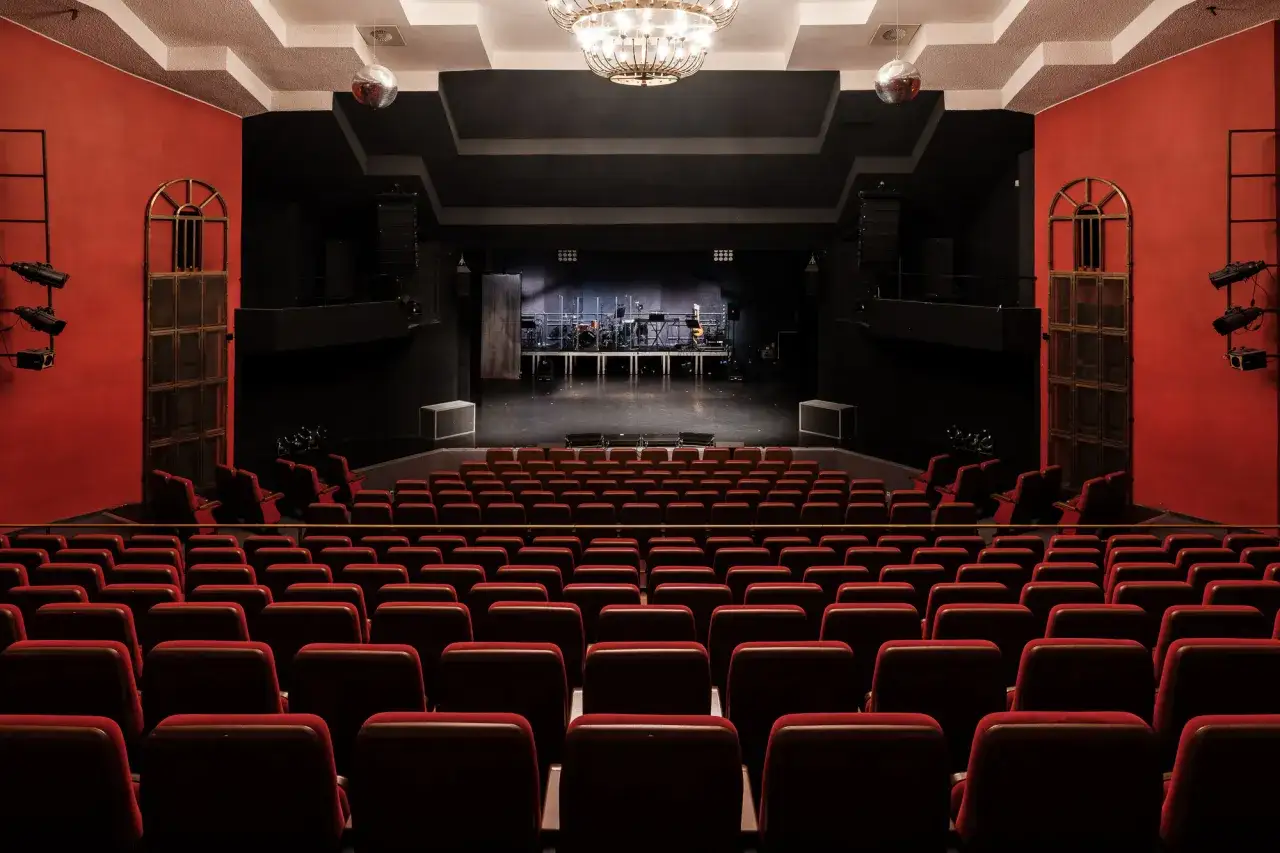 Pusta sala teatralna z czerwonymi fotelami i sceną gotową na repertuar teatru Rampa.
