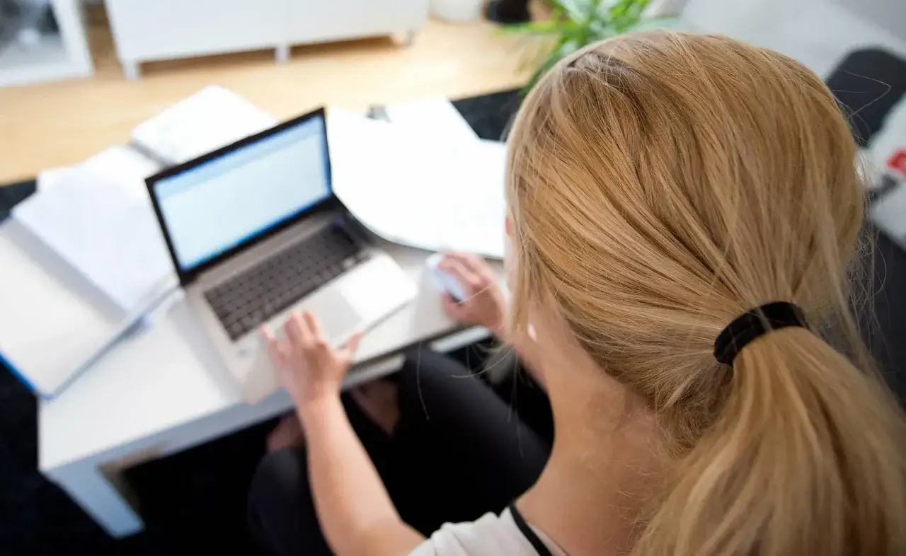 Frau mit blondem Pferdeschwanz arbeitet am Laptop. Sie hat eine **schwerbehinderung teilzeit bei vollem lohnausgleich** und ist im Homeoffice.