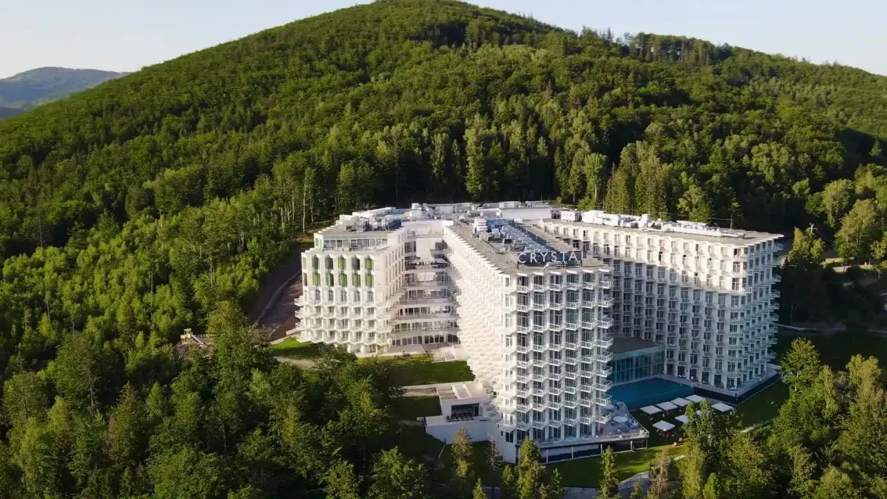 Nowy hotel w Wiśle, Crystal Mountain, wtopiony w zielone zbocze góry. Nowoczesna architektura z licznymi balkonami i basenem.