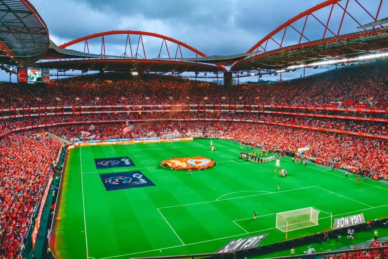 Stadion pełen kibiców w czerwonych barwach, gotowych do dopingu dla swojego klubu piłkarskiego z Lizbony.
