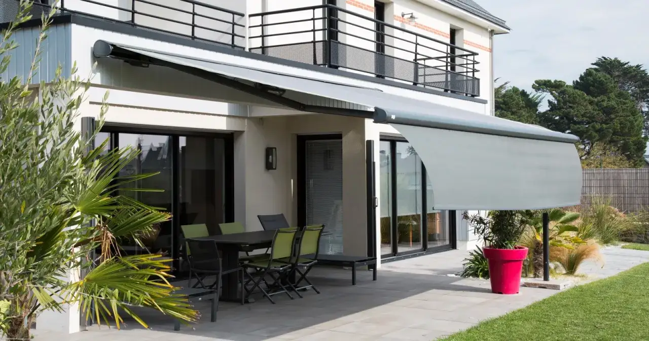 Un store banne gris prot&egrave;ge une terrasse moderne avec mobilier de jardin. Parfait pour profiter de l'ext&eacute;rieur.