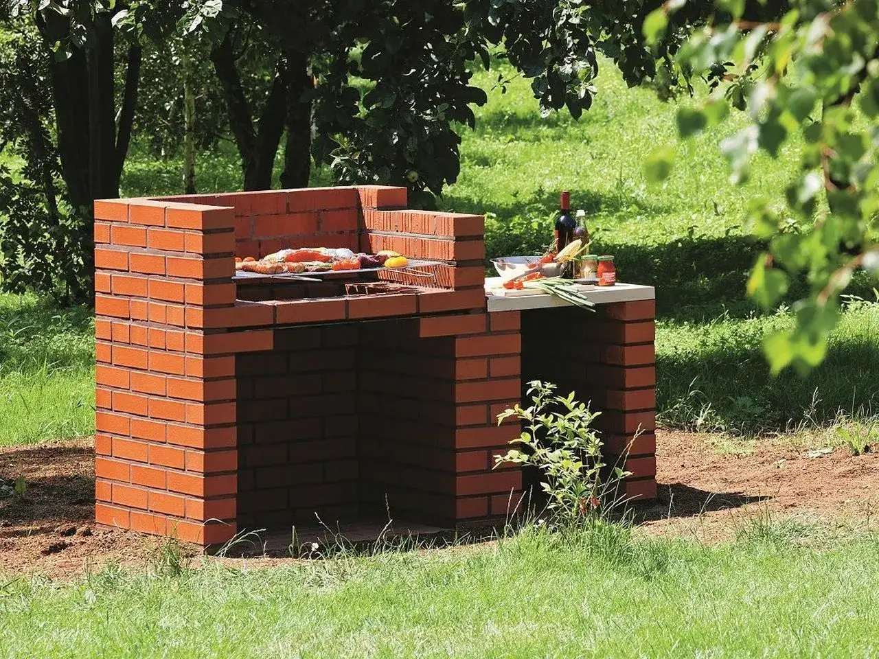 Solidny grill murowany z cegły, projekt gotowy do użycia. Na ruszcie ryba i warzywa, obok butelka wina.