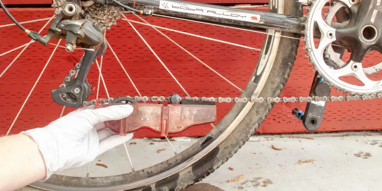 Rękawiczka w białej rękawiczce czyści łańcuch roweru za pomocą czerwonego narzędzia. Prawidłowe smarowanie roweru to klucz do płynnej jazdy.
