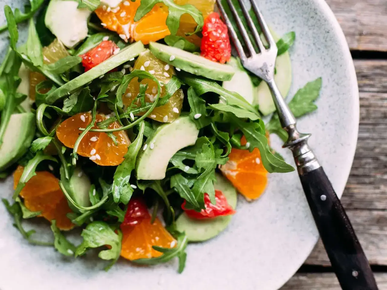 Salade de crudit&eacute;s color&eacute;e avec avocat, orange, pamplemousse et roquette, parsem&eacute;e de graines de s&eacute;same. Une fourchette est pos&eacute;e sur l'assiette.