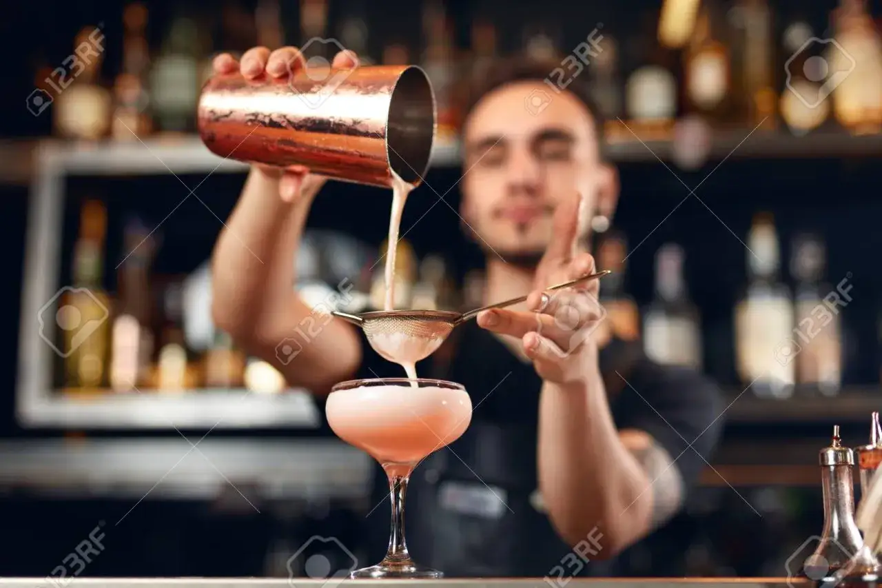Barman nalewający drinka do szklanki używając jiggera
