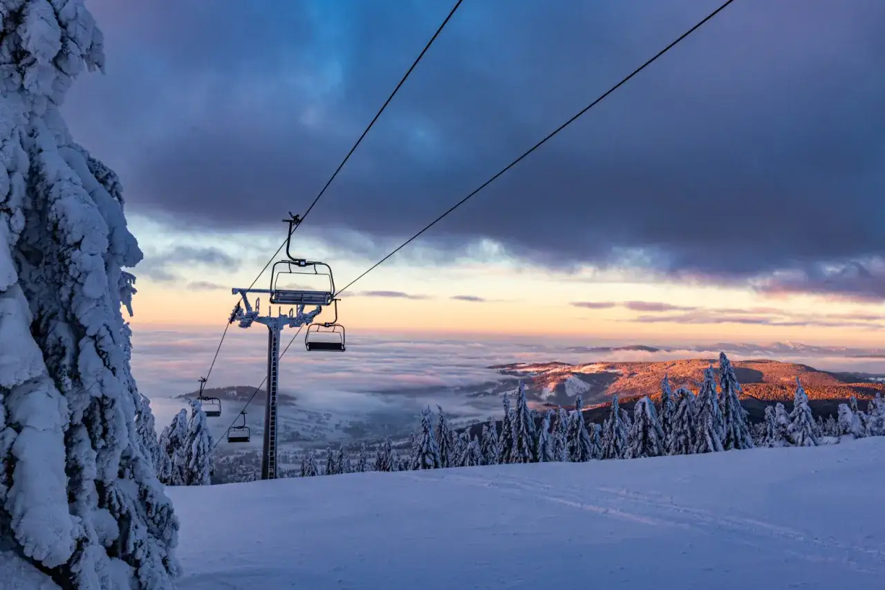 Krzesełka na tle zachodzącego słońca nad morzem chmur. Idealne miejsce na jazdę w **Rokytnice nad Jizerou snowpark** po całym dniu na stoku.