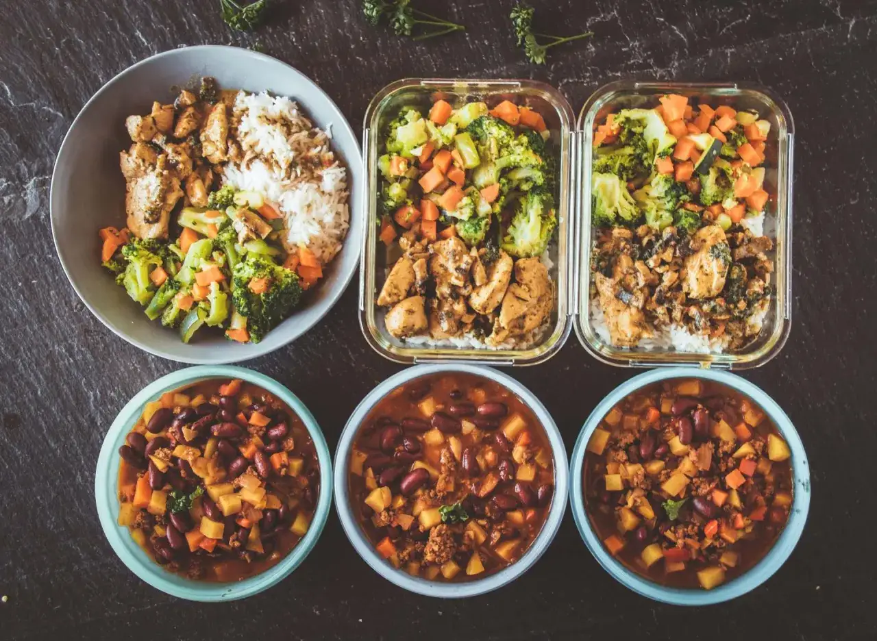 Vorbereitete Mahlzeiten: H&auml;hnchen mit Reis und Gem&uuml;se in Schalen, daneben drei Portionen Chili con Carne. Perfekt f&uuml;r Meal Prep!