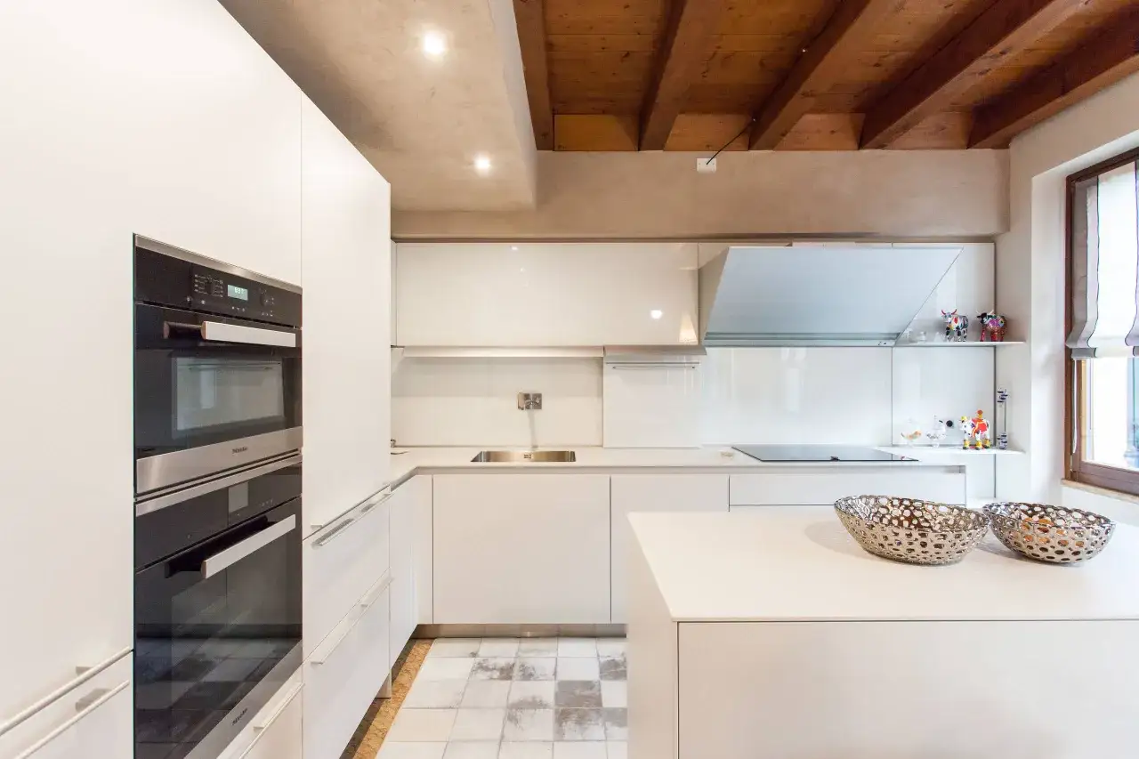 Cucina moderna con elettrodomestici a scomparsa e soffitto a travi a vista. L'altezza minima soffitto &egrave; valorizzata da faretti incassati.