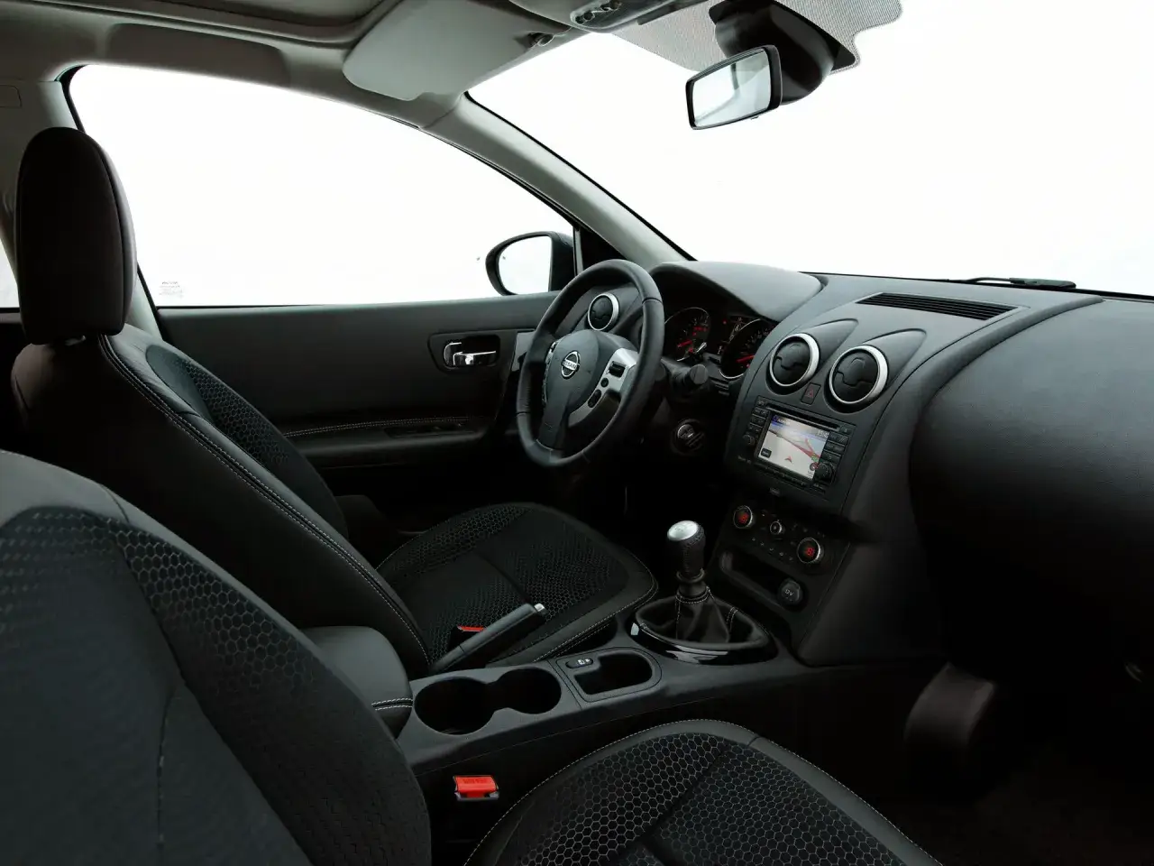 Wnętrze Nissan Qashqai 1. Widok na deskę rozdzielczą, kierownicę, fotele i konsolę środkową.