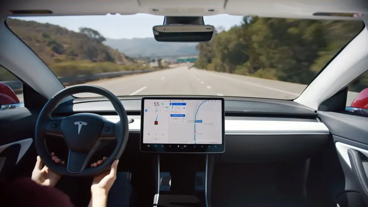 Wnętrze Tesli z widokiem na drogę. Kierownica z logo T, duży ekran nawigacji. Tesla to firma znana z innowacyjnych samochodów elektrycznych.