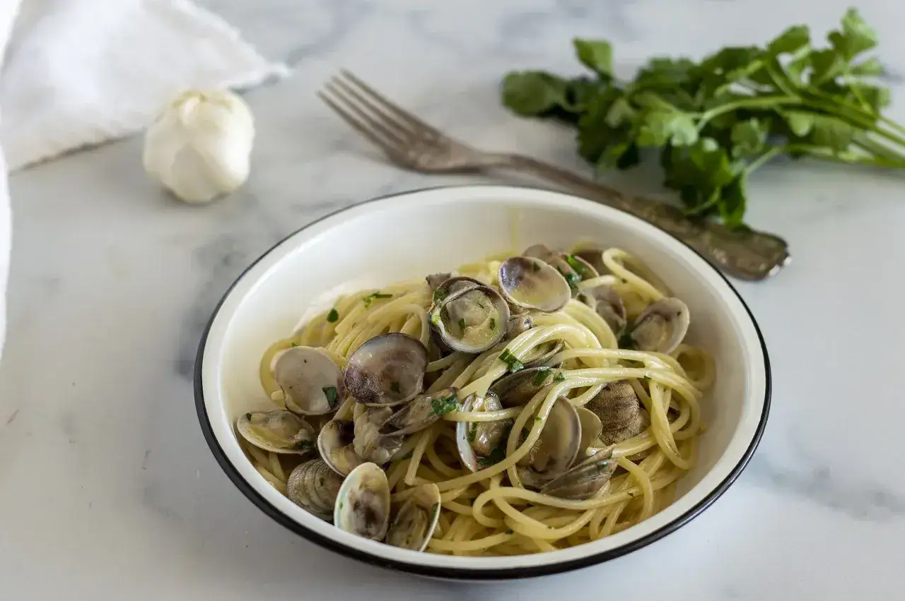 Un piatto invitante di linguine alle vongole, con aglio e prezzemolo freschi sullo sfondo.