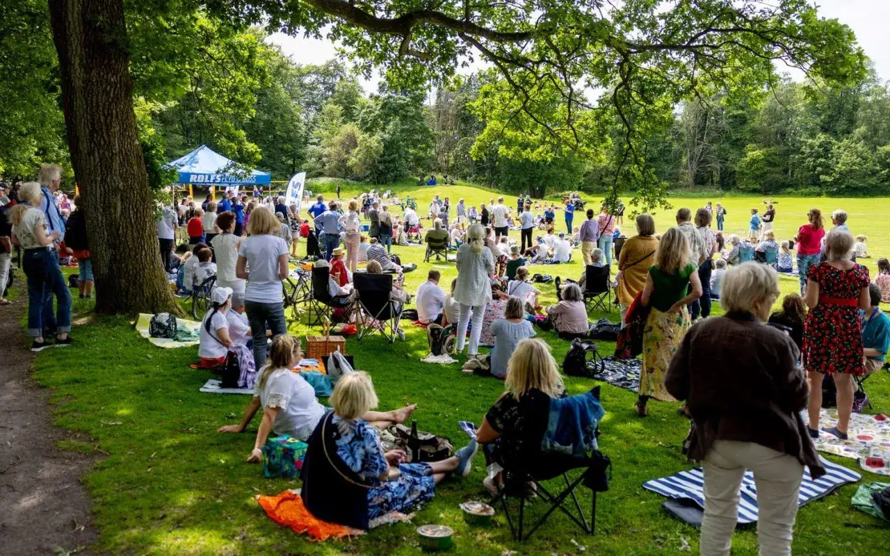 Midsommar i Slottsskogen lockar m&aring;nga till picknick i det gr&ouml;na. Folk sitter p&aring; filtar och stolar under tr&auml;dens skugga.