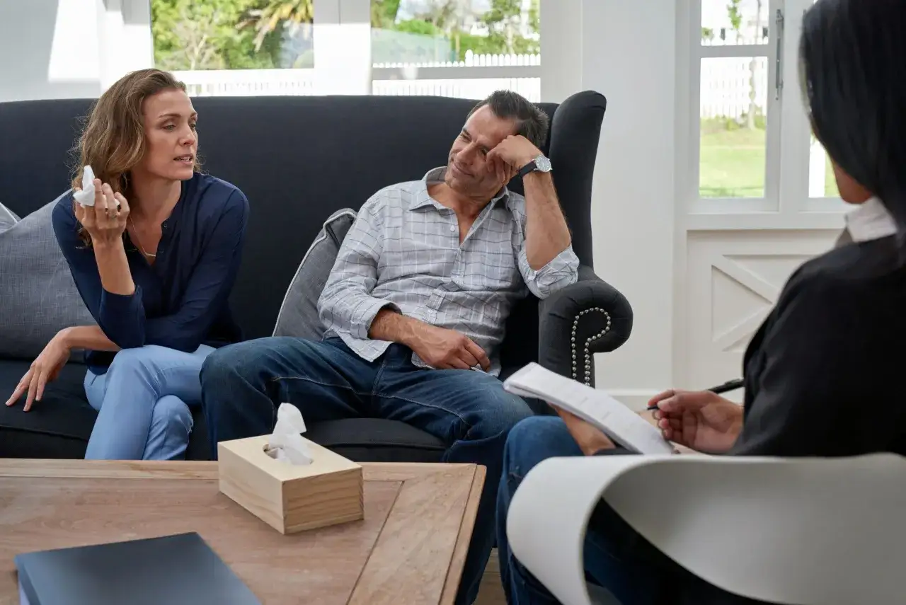 Un couple discute avec un thérapeute, la femme tient un mouchoir, le début d'une thérapie de couple.