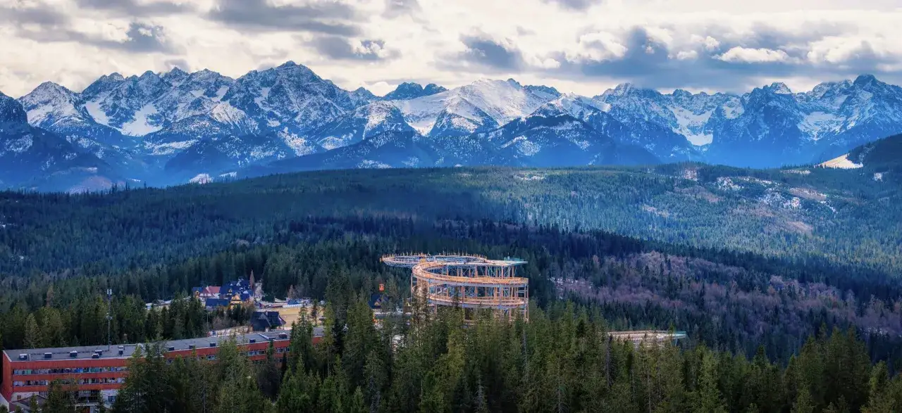 Drewniana konstrukcja ścieżki w koronach drzew na tle ośnieżonych Tatr. Sprawdź sky walk cennik i zaplanuj wizytę!