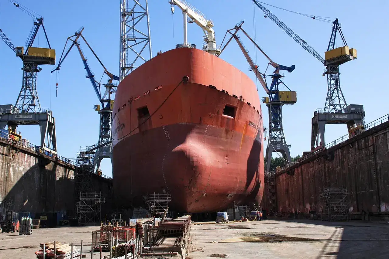 Gros plan sur la proue d'un navire rouge dans une cale s&egrave;che, entour&eacute; de grues. Le support bateau cale s&egrave;che est pr&ecirc;t pour la maintenance.