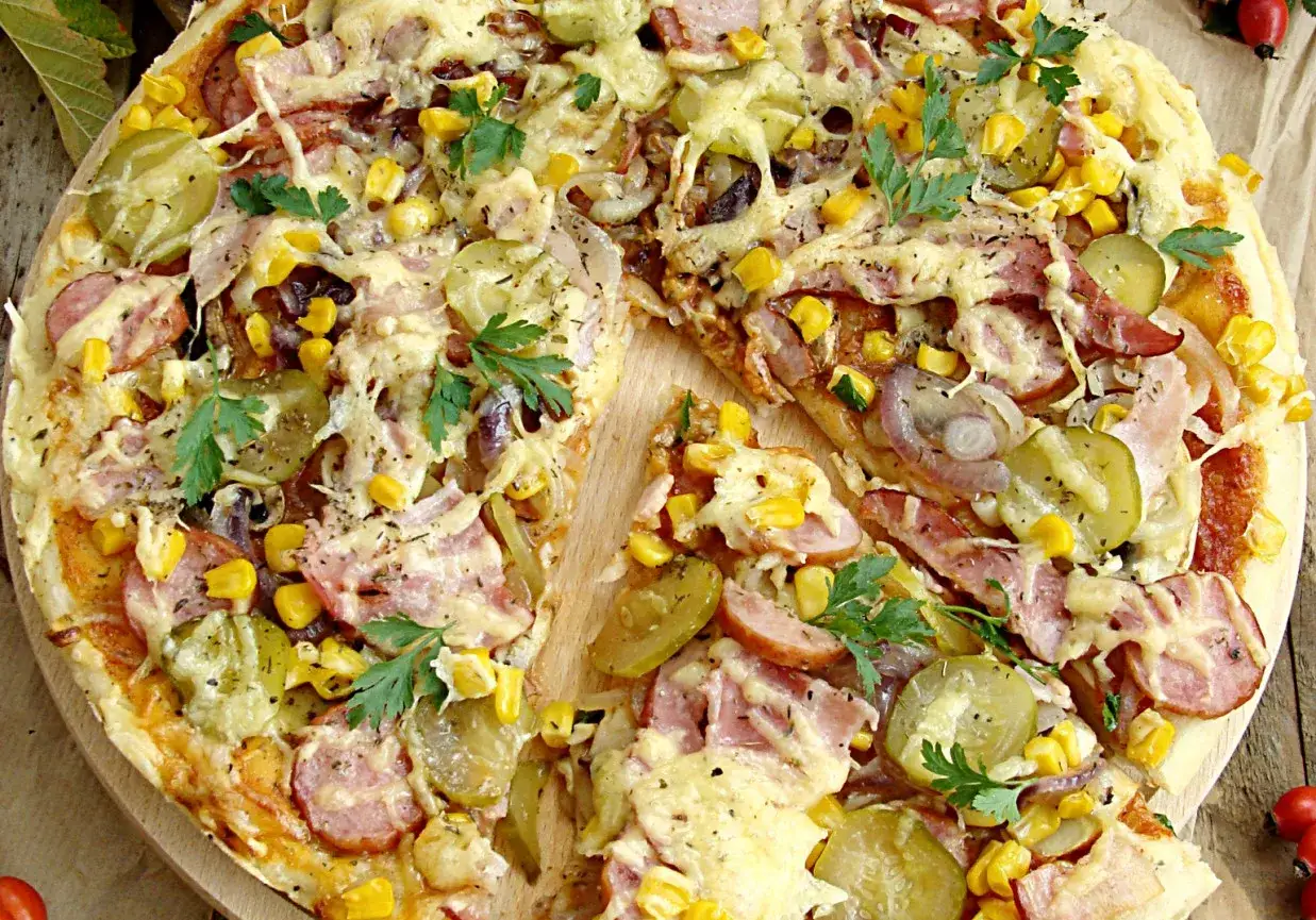 Pizza wiejska z chrupiącym boczkiem, kukurydzą, ogórkiem kiszonym i cebulą. Składniki tworzą apetyczną kompozycję.