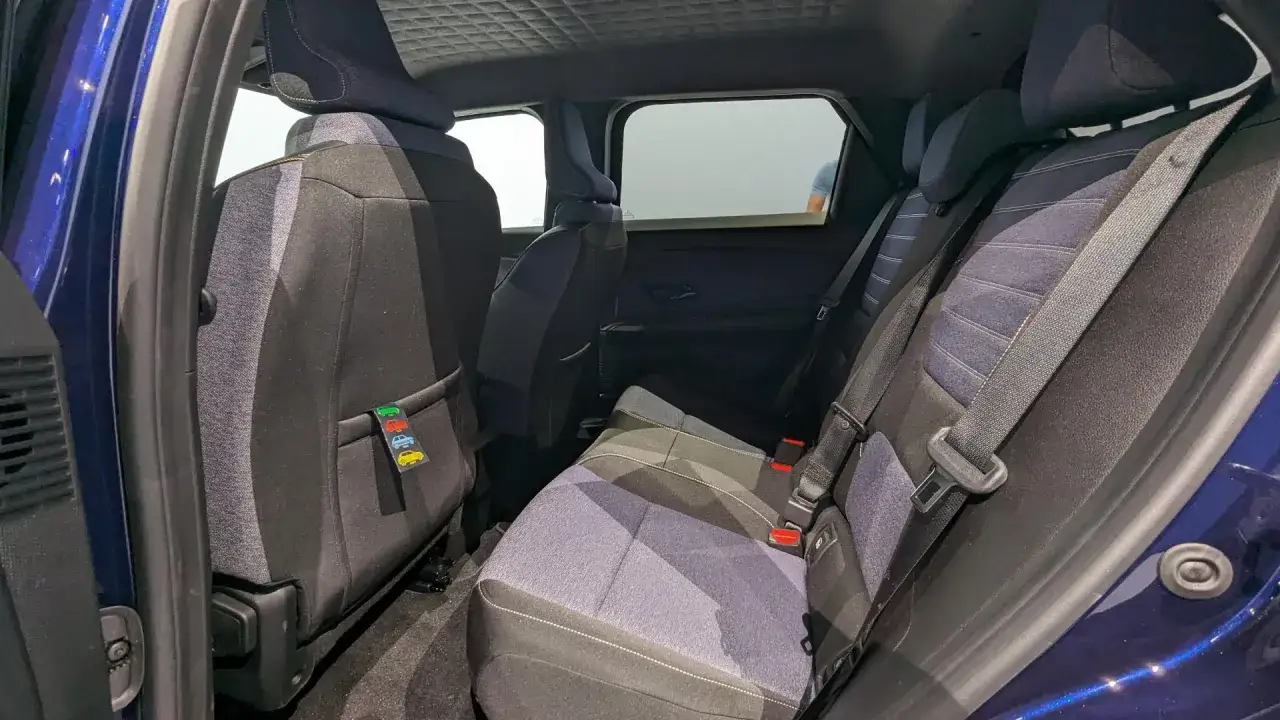 Int&eacute;rieur d'une voiture bleue, si&egrave;ges arri&egrave;re en tissu gris et bleu, avec une &eacute;tiquette d&eacute;corative de petites voitures. L'espace sugg&egrave;re le confort d'une dimension R5 &eacute;lectrique.