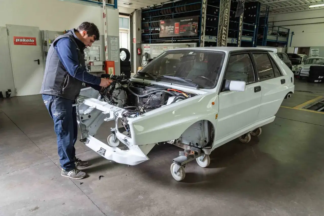 Meccanico lavora su un'auto da corsa bianca, con cablaggi esposti. La revisione scaduta è un problema comune per i veicoli d'epoca.
