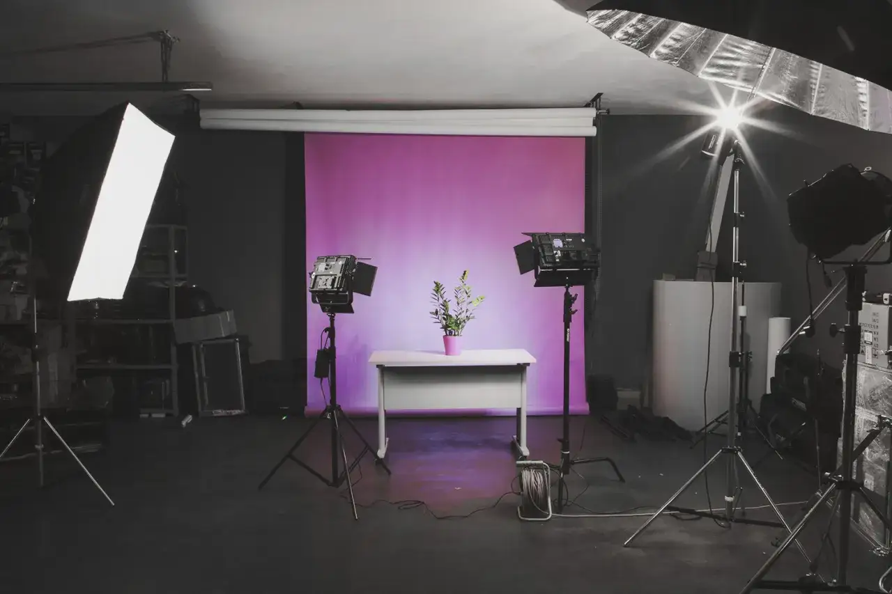 Studio do sesji produktowej. Różowe tło, biurko z rośliną, lampy studyjne. Idealne miejsce, by dowiedzieć się, jak zrobić zdjęcie produktu.