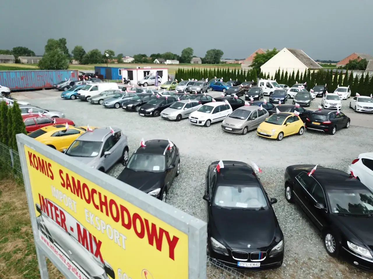 Komis samochodowy oferuje auta do 40 tys. zł. Wiele modeli, w tym czarne BMW i żółty Fiat, czeka na nowych właścicieli.