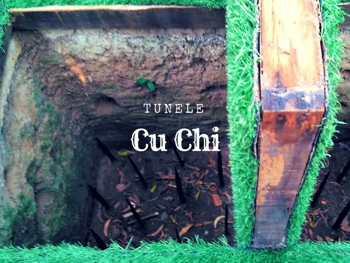 Wejście do tuneli Cu Chi, z ostrymi zaostrzonymi palikami w dole. Sztuczna trawa otacza drewniane belki.