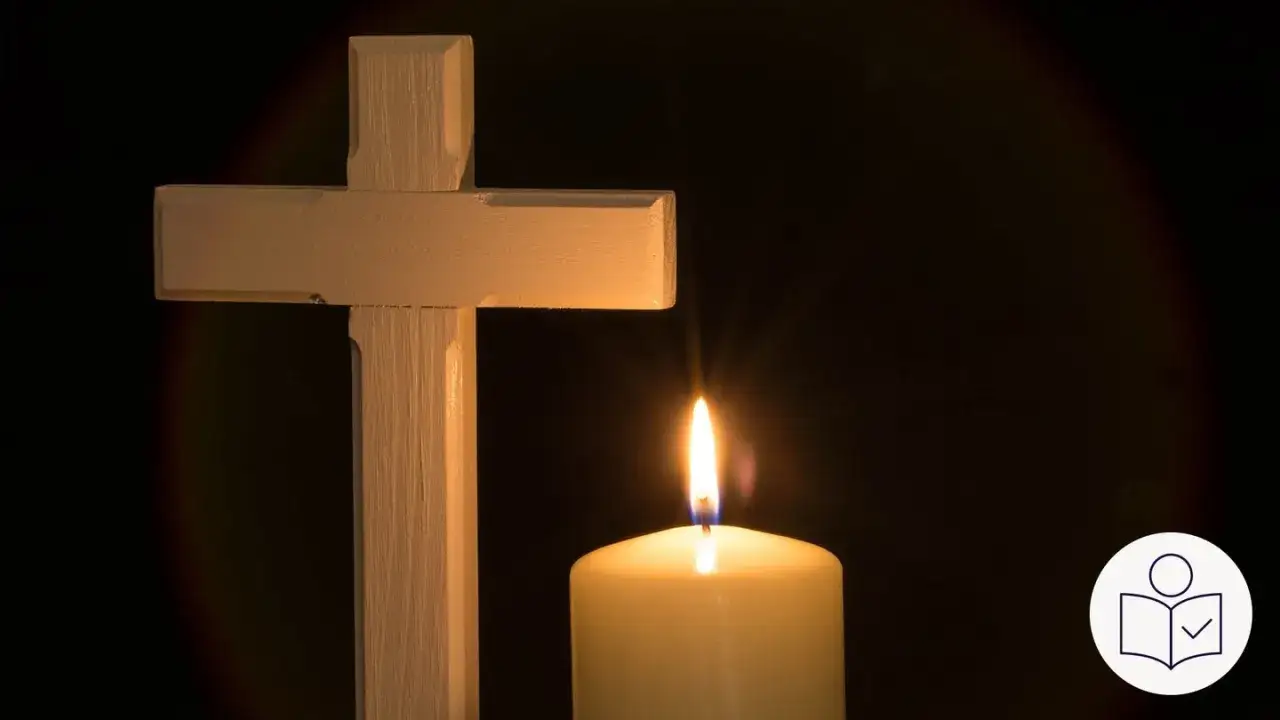 Ein Holzkreuz und eine brennende Kerze im Dunkeln, die an Karfreitag an die Bibelverse erinnert.