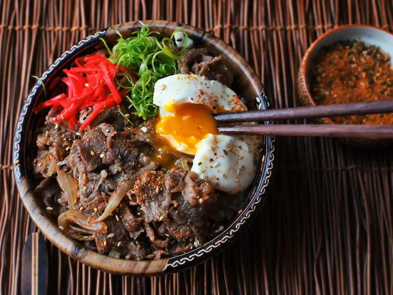 A delicious wagyu donburi with a perfectly runny egg yolk, topped with red pickled ginger and green onions.